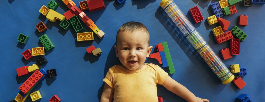 Happy baby playing with toy blocks in the kindergarten.